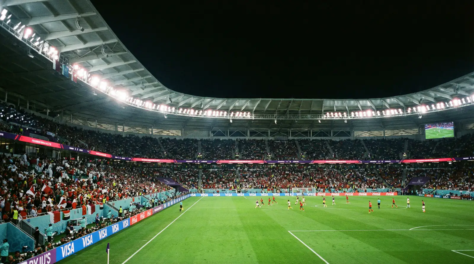 Modern football stadium illuminated by floodlights during a night-time World Cup fixture with the pitch glowing green under artificial light